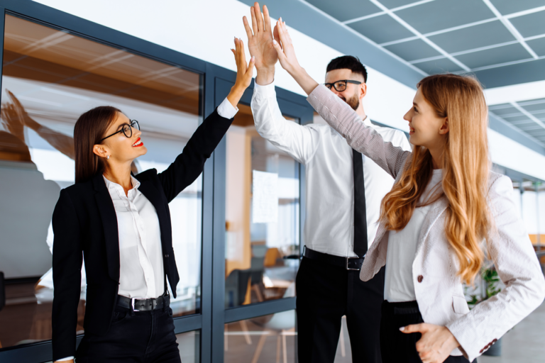 Drei Geschäftspersonen geben sich vor einem Büro mit 'ROCTOR'-Logo einen High-Five, symbolisieren Teamarbeit und schnelle Lieferung